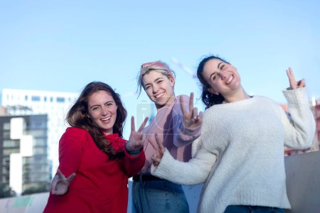 Three cheerful young women enjoy a sunny day outdoors, playfully posing with peace signs for the camera, exuding joy and camaraderie