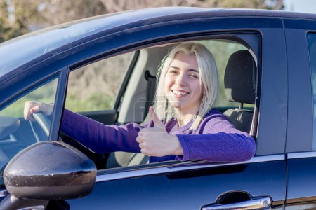 Photo for A smiling woman in a car giving a thumbs up, possibly indicating a good driving experience or satisfaction with a new car. - Royalty Free Image
