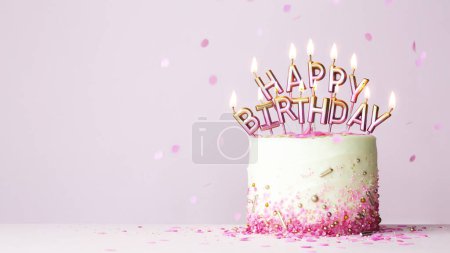 Foto de Pastel de cumpleaños de celebración con velas de cumpleaños rosas y doradas ortografía feliz cumpleaños contra un fondo rosa - Imagen libre de derechos