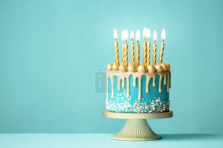 Elegante türkisfarbene Geburtstagstorte mit goldenem Tropfenglas und goldenen Geburtstagskerzen vor türkisfarbenem Hintergrund