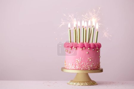 Pastel de cumpleaños rosa con velas de cumpleaños de oro y chispas de celebración sobre un fondo rosa liso
