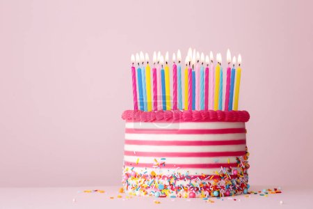 Foto de Pastel de cumpleaños decorado con crema de mantequilla a rayas rosa y blanca y muchas velas de cumpleaños sobre un fondo rosa - Imagen libre de derechos