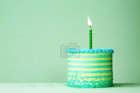 Foto de Pastel de cumpleaños rayado verde y azul con una vela de cumpleaños de celebración sobre un fondo verde liso - Imagen libre de derechos