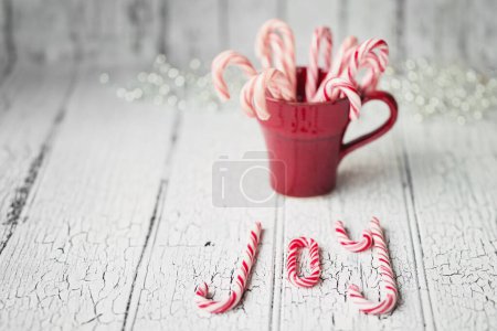 Foto de Taza roja llena de bastones de caramelo deletreando alegría sobre un fondo blanco - Imagen libre de derechos