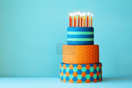 Photo for Brightly colored birthday cake covered with fondant, three tiers and colorful birthday candles - Royalty Free Image