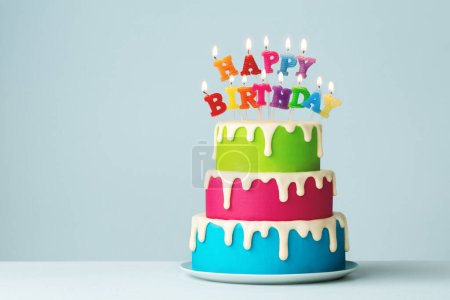 Colorful tiered birthday cake with colorful happy birthday candles and drip icing