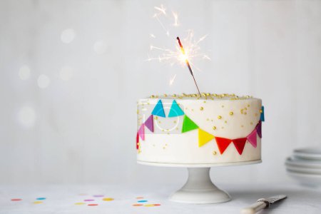 Foto de Pastel de cumpleaños de celebración con coloridos banderines de arco iris y una celebración chispeante - Imagen libre de derechos
