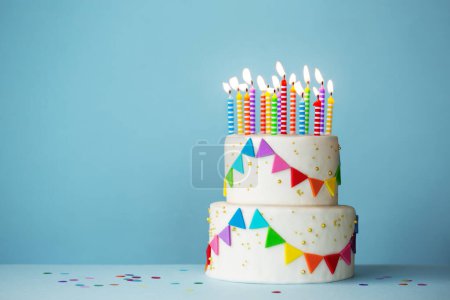 Photo for Tiered celebration birthday cake with colorful celebration bunting and birthday candles against a blue background - Royalty Free Image
