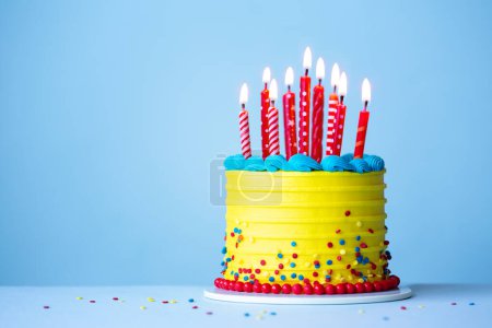 Foto de Colorido pastel de cumpleaños de celebración con glaseado amarillo y velas de cumpleaños rojas sobre un fondo azul - Imagen libre de derechos