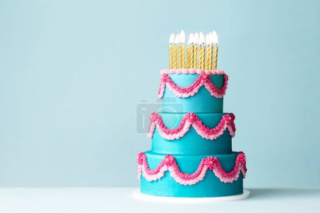 Tiered celebration birthday cake with pink ornate piped buttercream frills and gold birthday candles