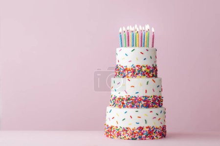 Tiered celebration birthday cake with colorful sugar sprinkles and twelve birthday candles