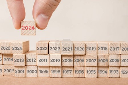 Photo for Photo of wooden block rows with gray numbers and one of them hold by a human hand with red number 2024 imprinted on wooden surface. New Year concept. - Royalty Free Image