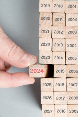 Photo for Photo of wooden block row with gray numbers and one of them hold by a human hand with red number 2024 imprinted on wooden surface. Gray backgound. New Year concept. - Royalty Free Image