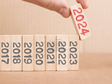 Photo for Photo of wooden block row with gray numbers and one of them hold by a human hand with red number 2024 imprinted on wooden surface. New Year concept. - Royalty Free Image