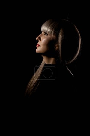 Foto de Hermosa chica con flequillo rubio franja contra fondo negro. Retrato lateral abstracto. - Imagen libre de derechos