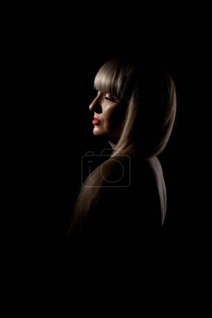 Foto de Hermosa chica con flequillo rubio franja contra fondo negro. Retrato lateral abstracto. - Imagen libre de derechos