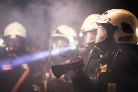 Groupe de pompiers professionnels. Pompiers et pompiers portant des casques de protection uniformes masques à oxygène et lampes de poche. Fumée dans l'atmosphère.