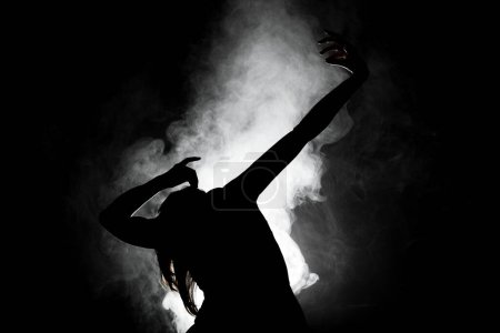 Silhouette modern ballet dancer posing on dark background with smoke