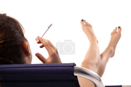 Foto de Hermosa chica joven en traje de baño relajante en la tumbona de verano y fumar cigarrillo aislado sobre fondo blanco. - Imagen libre de derechos