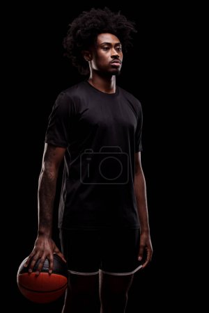 Foto de Basketball player holding a ball. Concentrated african american sports man against black background. - Imagen libre de derechos