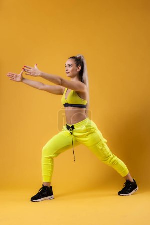 Foto de Hermosa chica en traje amarillo bailando zumba. Instructor de baile feliz sobre fondo amarillo oscuro o naranja. - Imagen libre de derechos