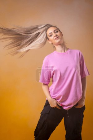 Foto de Hermosa chica rubia en camisa rosa bailando contra el humo y la niebla de fondo amarillo. - Imagen libre de derechos