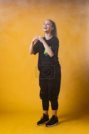 Foto de Hermosa chica en traje negro sonriendo. Instructor de baile feliz sobre fondo amarillo oscuro o naranja. - Imagen libre de derechos