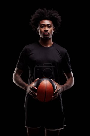 Foto de Basketball player holding a ball. Concentrated african american sports man against black background. - Imagen libre de derechos