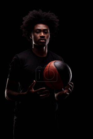 Portrait of a basketball player. African American man in sports uniform with basket ball posing against black background.