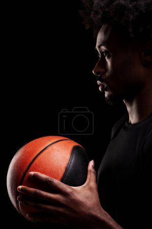 Basketball player holding a ball. Concentrated african american sports man against black background.