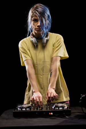 Chica con auriculares se centra en la mezcla de música en una caja de resonancia. DJ femenino con pelo azul y camiseta amarilla.