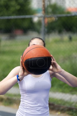 Girl playing basketball. Player throwing ball. Outdoor sports field in urban surroundings.