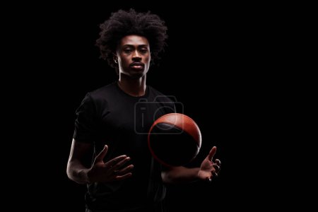 Portrait of a basketball player. African American man in sports uniform with basket ball posing against black background.
