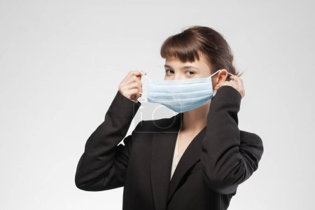 Photo for Portrait of a young woman in business attire adjusting a blue medical mask, symbolizing health precautions in professional settings. - Royalty Free Image