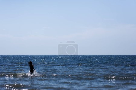 Ein heiteres Bild einer Person, die im riesigen Ozean steht, während das Sonnenlicht auf dem Wasser glitzert, unter einem riesigen blauen Himmel.