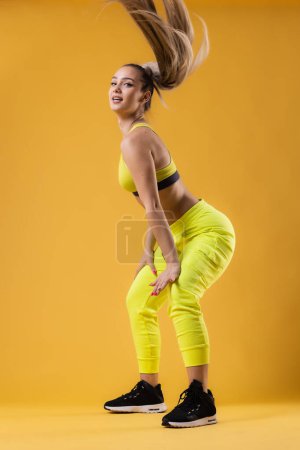 Belle fille en tenue jaune dansant zumba. Joyeux instructeur de danse sur fond jaune foncé ou orange.