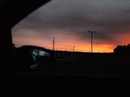Téléchargez les photos : Haute tension électrique tour ciel coucher de soleil paysage, arrière-plan industriel de la fenêtre de la voiture. - en image libre de droit