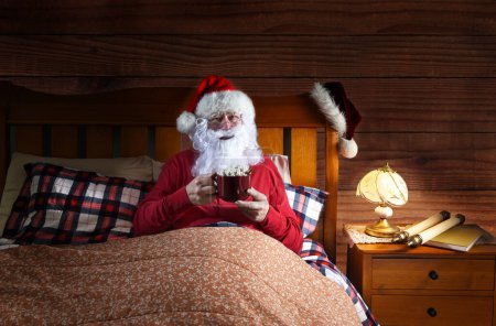 Photo for Santa Claus Laying in bed with a large mug of hot cocoa. - Royalty Free Image