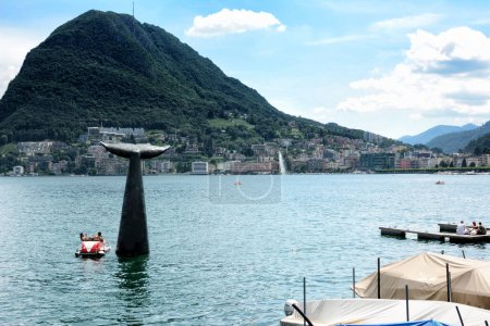 Photo for LUGANO, SWITZERLAND - 5 JUL 2014: People in pedal boats pause and take selfies at the Whale Tail Sculpture in Lake Lugano. - Royalty Free Image