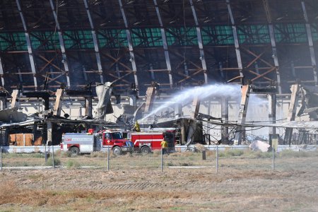 Foto de TUSTIN, CALIFORNIA - 8 NOV 2023: OCFA Equipos de bomberos colocando agua en un punto caliente en llamas en el Hangar MCAS Tustin Blimp, el día después de que comenzó el incendio. - Imagen libre de derechos
