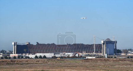 Foto de TUSTIN, CALIFORNIA - 8 NOV 2023: OCFA Jet en aproximación al aeropuerto John Wayne vuela sobre el Hangar MCAS Tustin Blimp, el día después de que comenzó el incendio. - Imagen libre de derechos