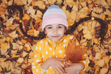 Téléchargez les photos : Belle petite fille jouant dans des feuilles d'automne colorées tombées dans un parc. Ginkgo biloba arbre. - en image libre de droit