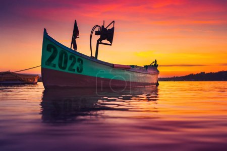 Foto de 2023 concepto de año nuevo. Barco de pesca en la orilla y ondulación de agua de mar en dramático atardecer colorido - Imagen libre de derechos