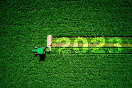 2023 Bonne année concept d'agriculture. Tracteur agricole rouge fauchage champ vert, vue aérienne