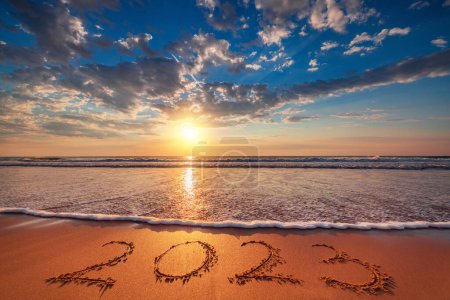 Happy New Year 2023 concept, lettering on the beach sand at sunrise. Ocean sunset. 