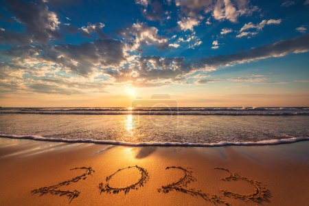 Foto de Feliz Año Nuevo 2023 concepto, letras en la arena de la playa del océano. Hermoso amanecer o puesta de sol sobre las olas del mar y la orilla. - Imagen libre de derechos