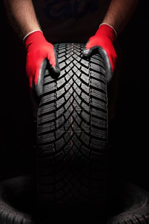 Foto de Servicio de neumáticos de coche y manos de mecánico sosteniendo neumático nuevo sobre fondo negro con espacio de copia para texto - Imagen libre de derechos