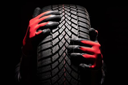 Téléchargez les photos : Service de pneus de voiture et les mains du mécanicien tenant un pneu neuf sur fond noir avec espace de copie pour le texte - en image libre de droit