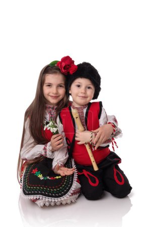 Bulgarian kids boy and girl in traditional folklore costumes with snowdrop flowers and handcraft wool bracelet martenitsa symbol of Baba Marta, spring and Easter, studio portrait. Martisor