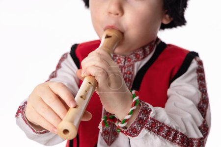 Foto de Niño músico búlgaro con flauta en traje folclórico tradicional con martenitsa símbolo de la primavera, Baba Marta y vacaciones de Pascua, retrato sobre fondo blanco, martisor - Imagen libre de derechos